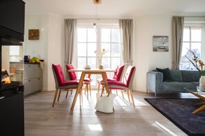 A modern living room with a dining area, a sofa, and a kitchen visible. - Reetdachhaus am Bodden mit Sauna (Fuhlendorf)