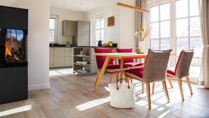 Una sala de estar moderna con chimenea, un comedor con sillas rojas y una cocina al fondo.