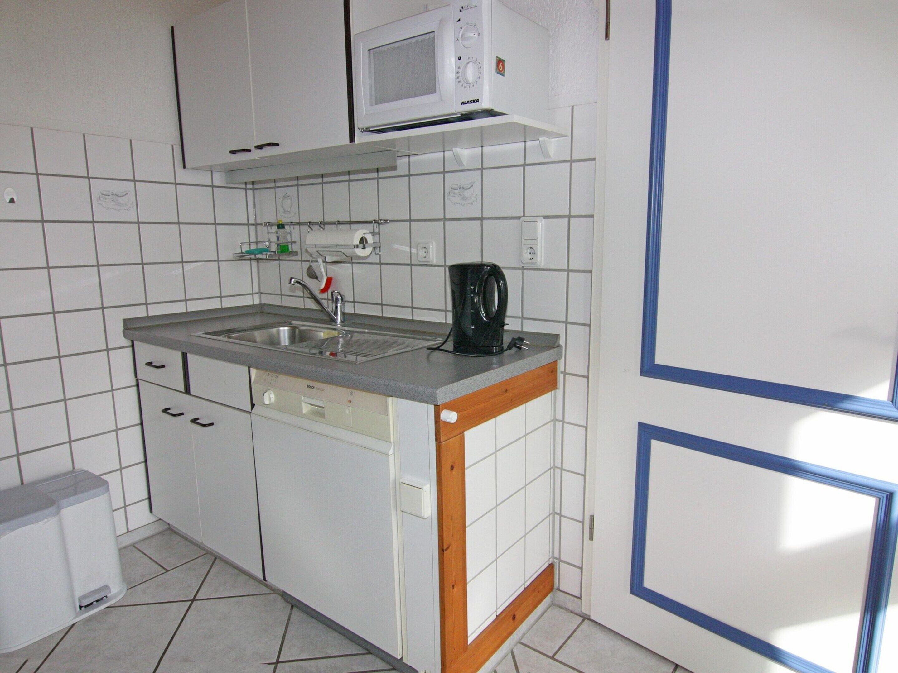 Een kleine keuken met witte kasten, een inbouwmagnetron, een spoelbak en een koffiezetapparaat.