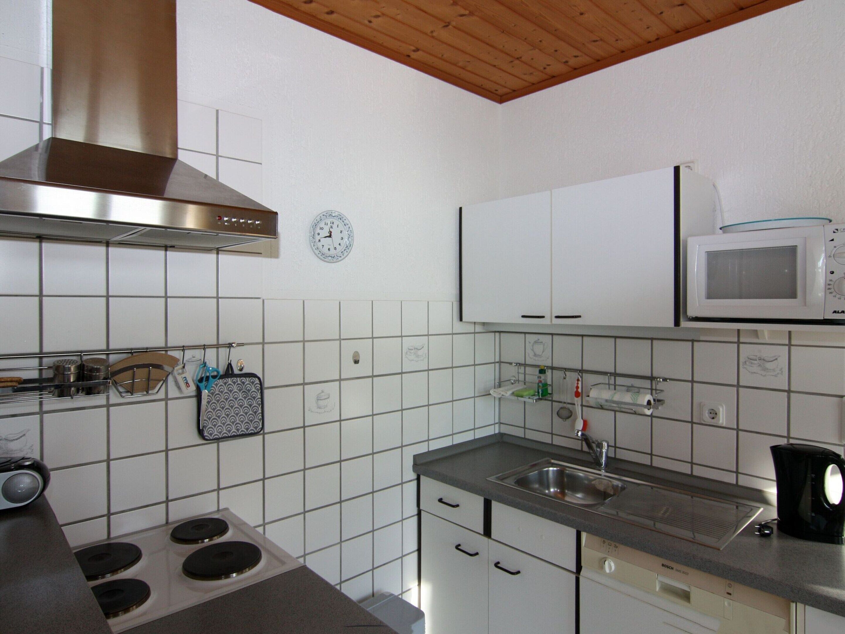 Una cucina con mobili bianchi, una cappa aspirante in acciaio inossidabile, un forno a microonde e un lavandino.