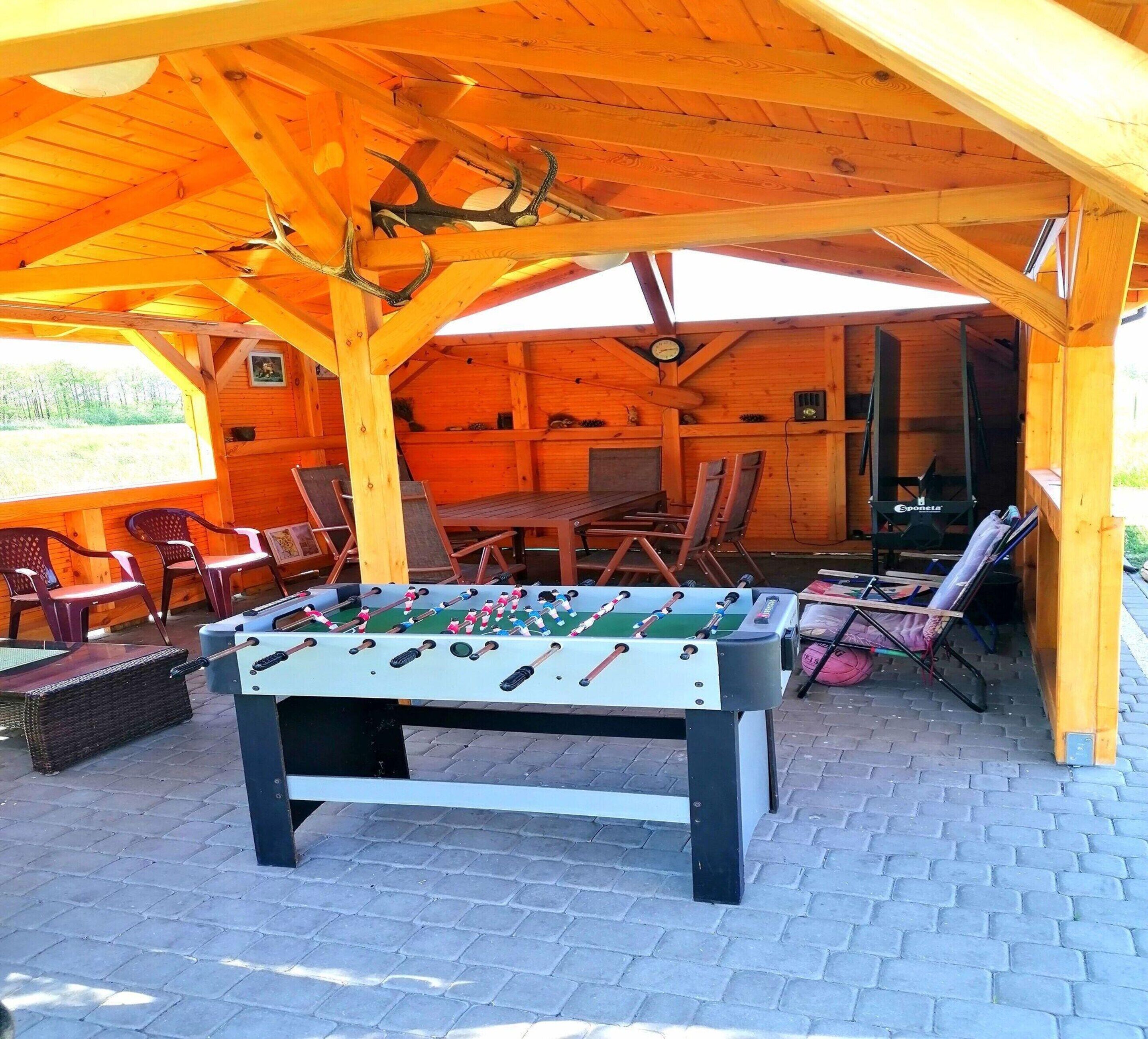 Ein hölzerner Außenbereich mit Tischfußball, Sitzgelegenheiten und einer Uhr an der Wand.