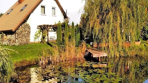 A house with a sloped roof, a pond with lily pads, and willow trees. - Holiday Apartment, 2 Bedrooms, Garden, Bicycles (Kołobrzeg)