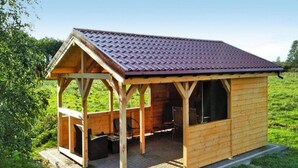 A wooden cabin with a tiled roof, a covered patio, and a small table and chair set. - Holiday Apartment, 2 Bedrooms, Garden, Bicycles (Kołobrzeg)
