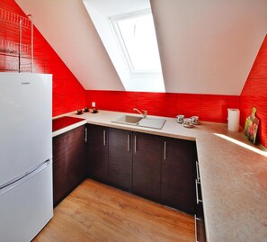 A compact kitchen with a skylight, a refrigerator, dark cabinets, and a wooden floor. - Holiday Apartment, 2 Bedrooms, Garden, Bicycles (Kołobrzeg)