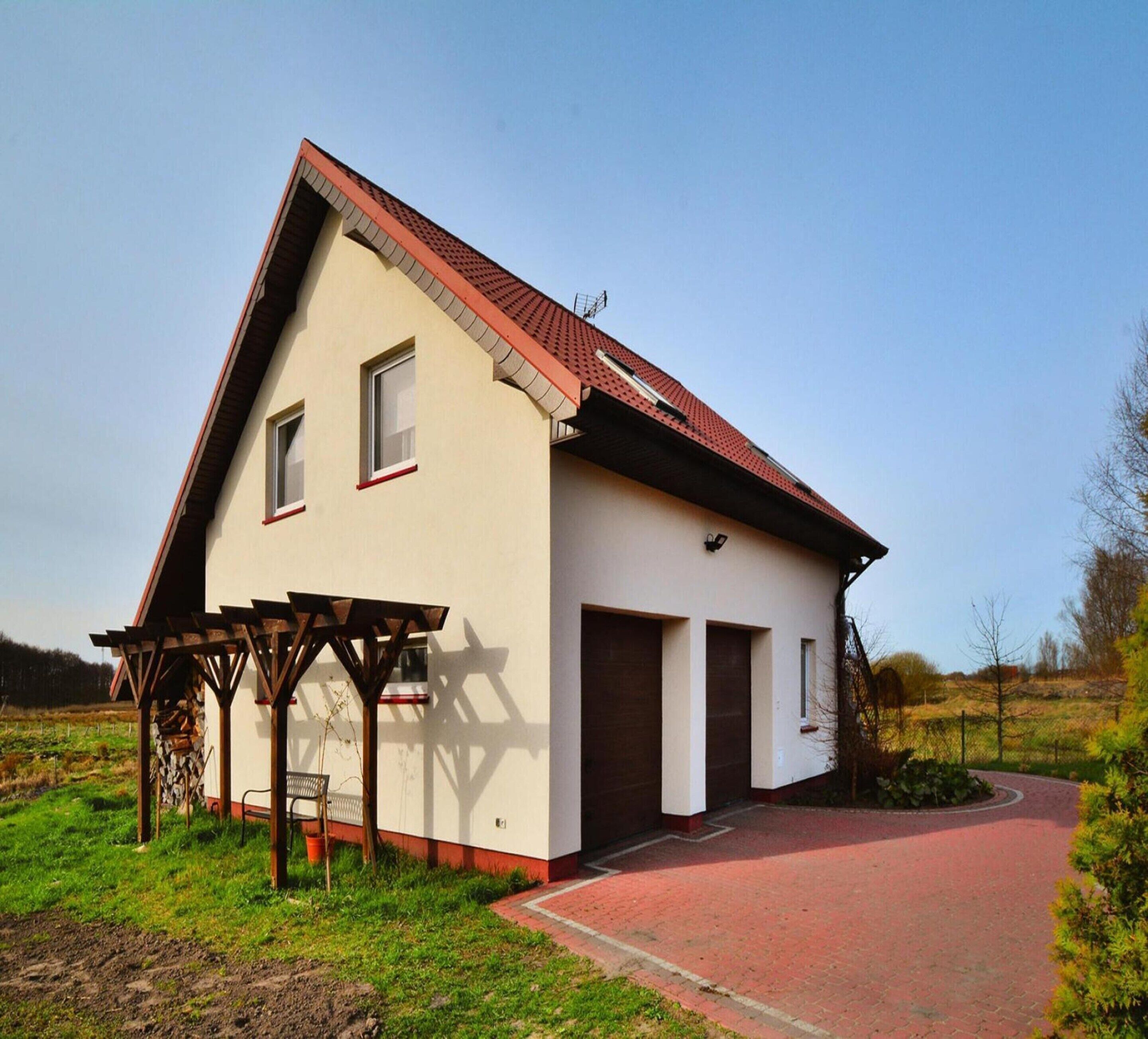 A single-story house with a red roof and beige walls, featuring a covered patio area with a bench.