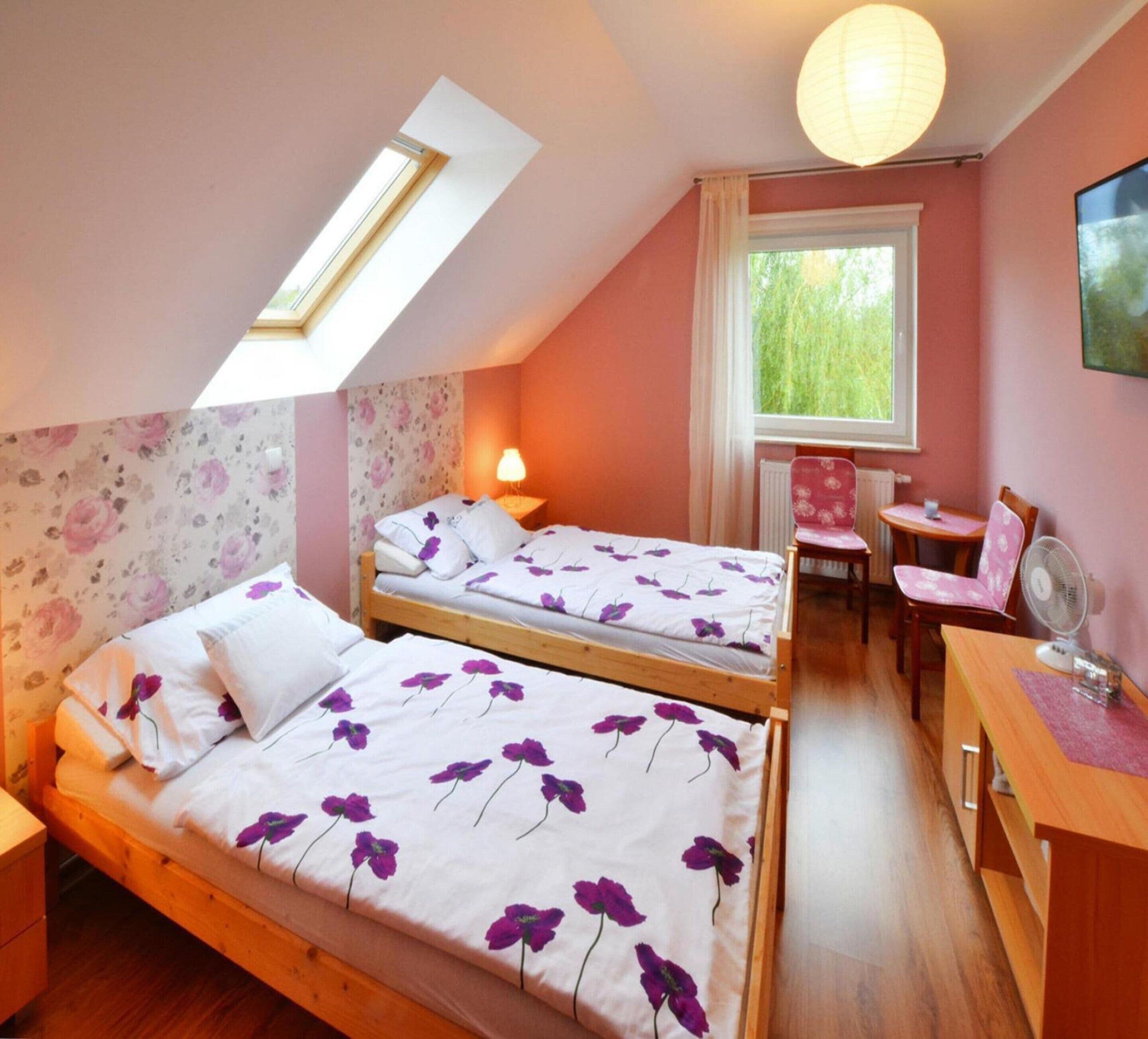 A bedroom with two beds, a desk, a chair, a window, and a skylight.