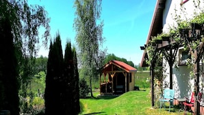 A wooden structure with a red roof, a grassy yard, and a body of water. - Holiday Apartment, 2 Bedrooms, Garden, Bicycles (Kołobrzeg)