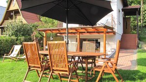 En utomhusplats med sittmöbler i trä, bestående av ett bord och stolar, ett parasoll och en pergola.