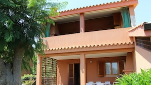 A two-story building with a balcony, a covered outdoor seating area, and a window with shutters. - Apartment in Costa Rei Near White Sandy Beach (Muravera)