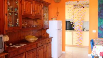 Una cocina con armarios de madera, un refrigerador blanco y una zona de comedor con una silla azul.