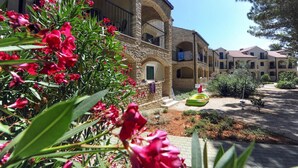A courtyard with a stone building featuring arched balconies, a garden with red flowers, and a clear blue sky. - Family Fun at Zaton Resort (Nin)