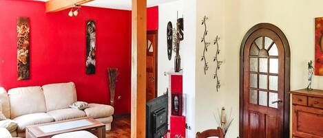 A living room with a red wall, a wooden ceiling, a white sofa, a wooden dining table, and a wooden door with glass panels.