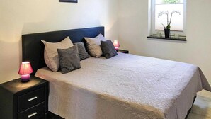 A neatly made bed with a patterned bedspread, two bedside lamps, and a window with a view of greenery.