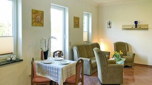 A dining area with a table set for four, two armchairs, a sofa, and a small side table with flowers.