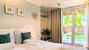 Un dormitorio con una cama grande, un reloj de pared, cuadros enmarcados y un ventanal corredero a un jardín.