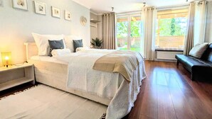 Un dormitorio con una cama grande, una mesita de noche con lámpara, un sofá y vistas al exterior con vegetación.
