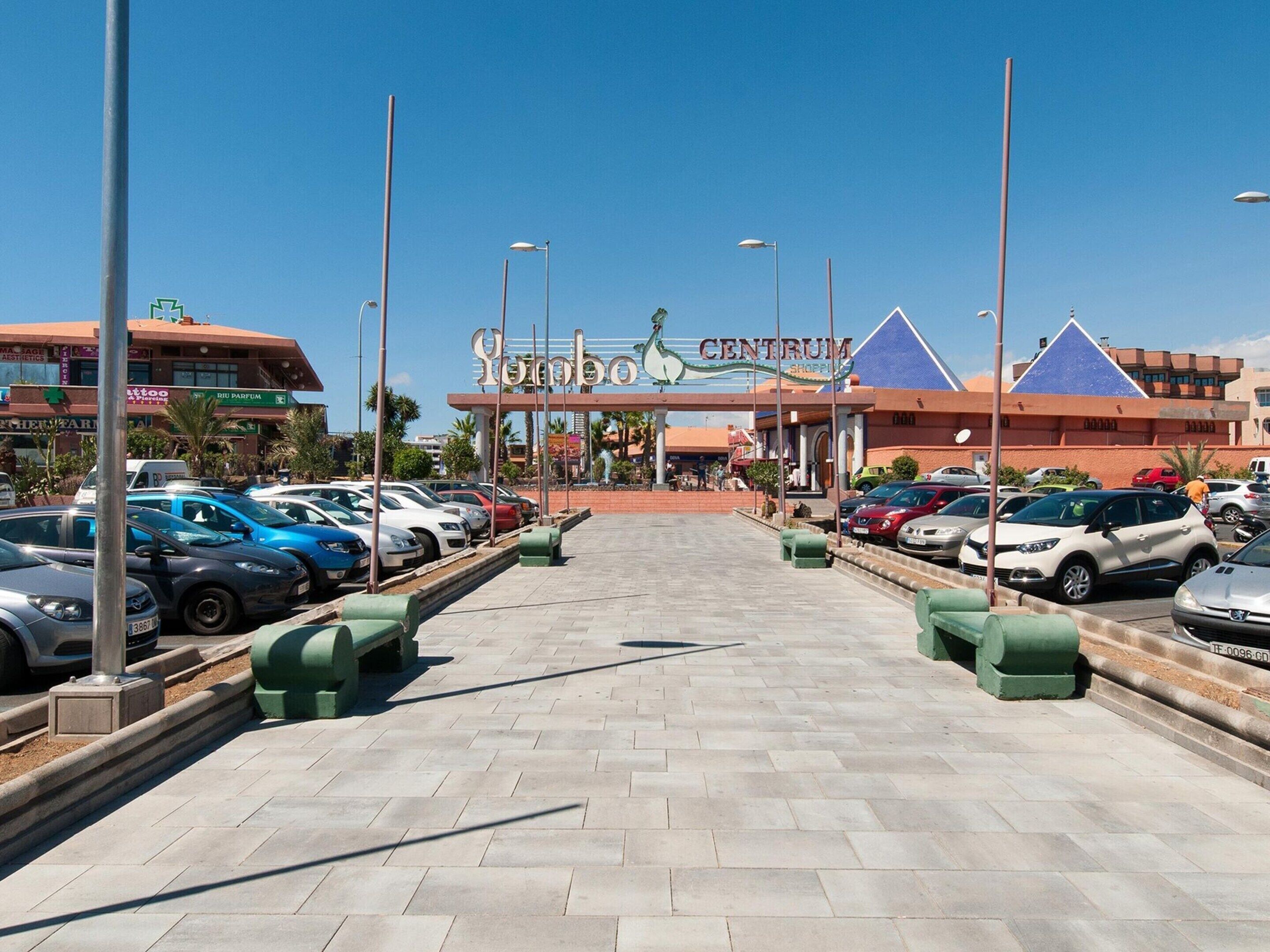 A parking lot leading to a shopping center with a prominent sign.