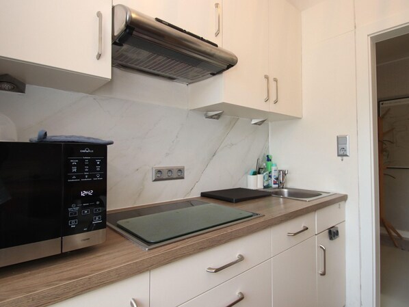 A modern kitchen with a built-in oven, a microwave, and a stainless steel range hood. - Doppelhaushalfte in Dornumersiel (Dornum)