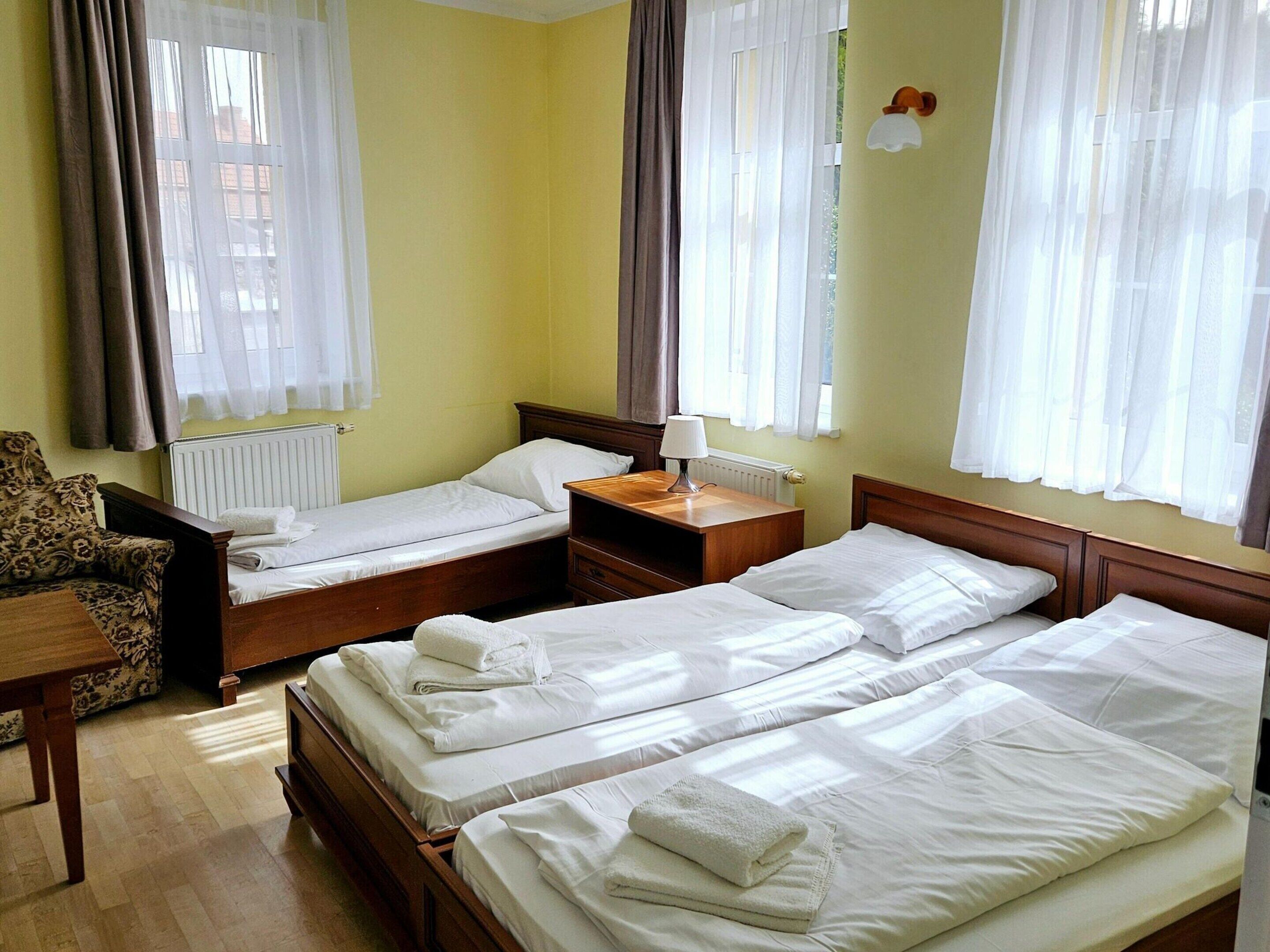 A hotel room with two single beds, a wooden nightstand, a chair, and a table.