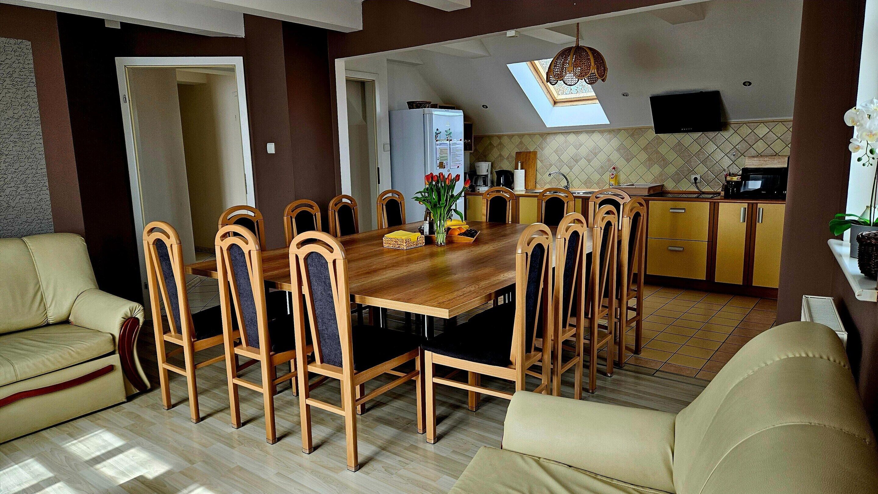 A dining area with a wooden table and chairs, a sofa, and a kitchen in the background.