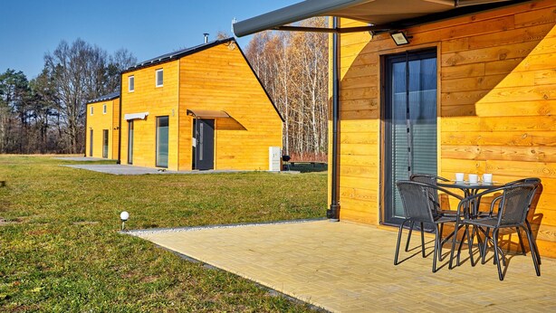 Un edificio moderno de madera con un porche cubierto y mobiliario exterior.
