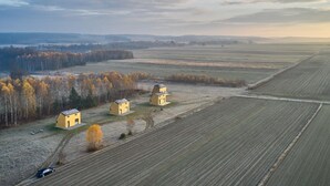 Paisaje rural con tres casas amarillas, campos abiertos y una línea de árboles distante.