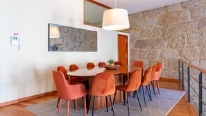 Een eetgedeelte met een stenen muur, een ronde houten tafel en oranje stoelen.