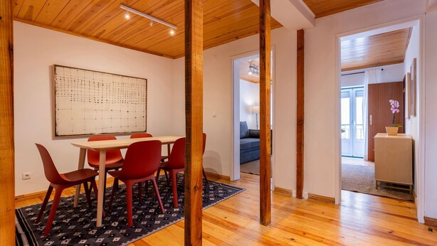 Una habitación con techo de madera, una mesa de comedor con sillas rojas, un tapete de diseño blanco y negro, y un cuadro abstracto grande en la pared.