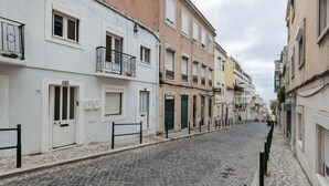 Una estrecha calle empedrada flanqueada por edificios de varios pisos, algunos con balcones y contraventanas.