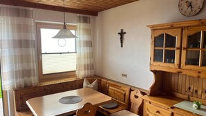 Une pièce chaleureuse avec une table à manger en bois, des chaises, un buffet en bois, une horloge et une fenêtre avec des rideaux.