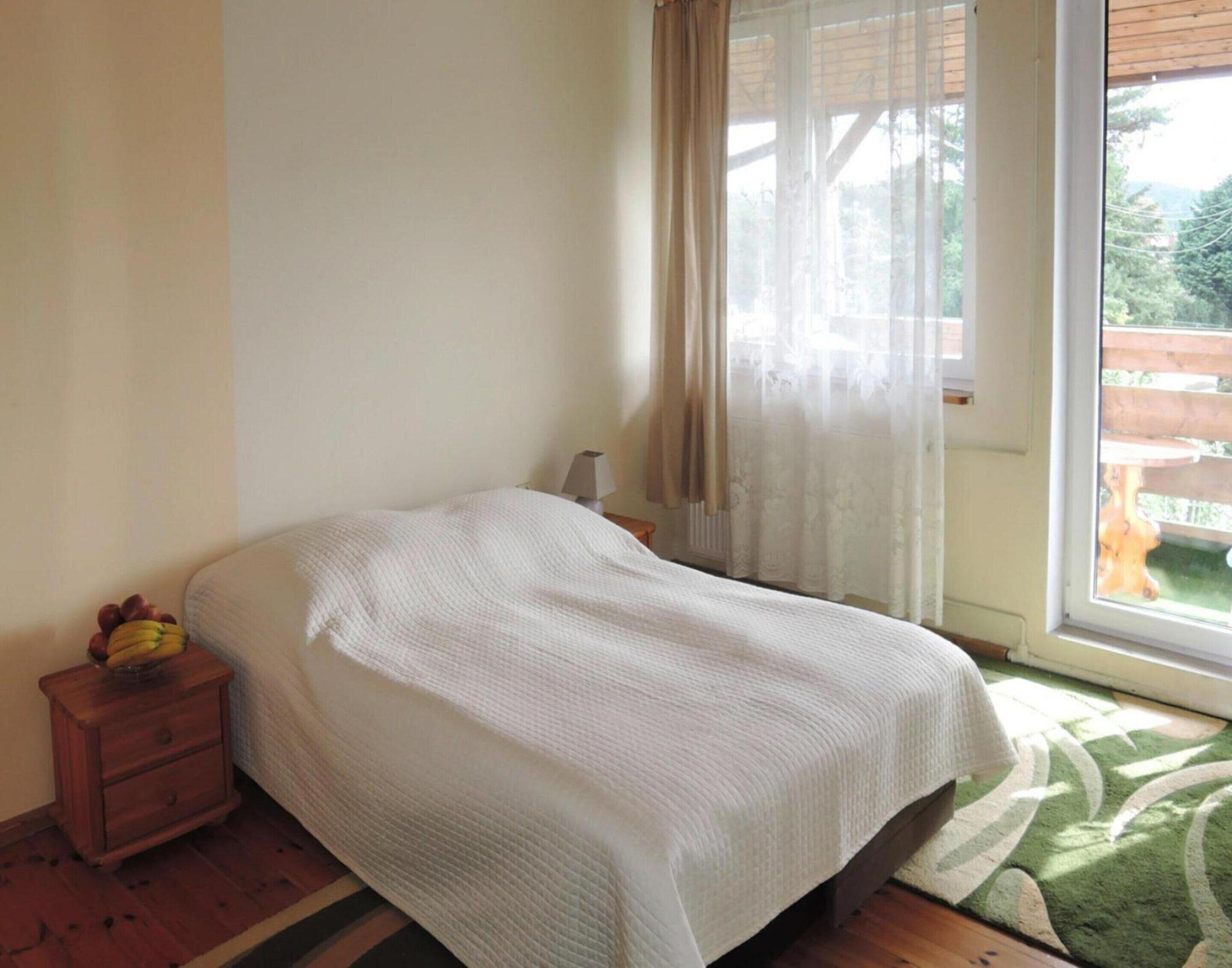 Une chambre à coucher avec un lit, une table de chevet, une lampe et une fenêtre avec des rideaux.