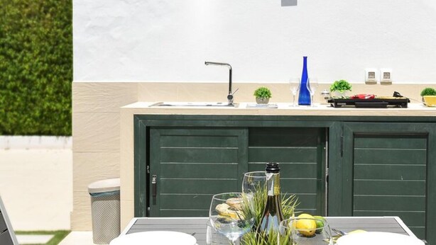 An outdoor kitchen area with a sink, a blue vase, and a bottle of wine on the counter. - Central Bungalow With Communal Pool in Maspalomas (San Bartolomé de Tirajana)