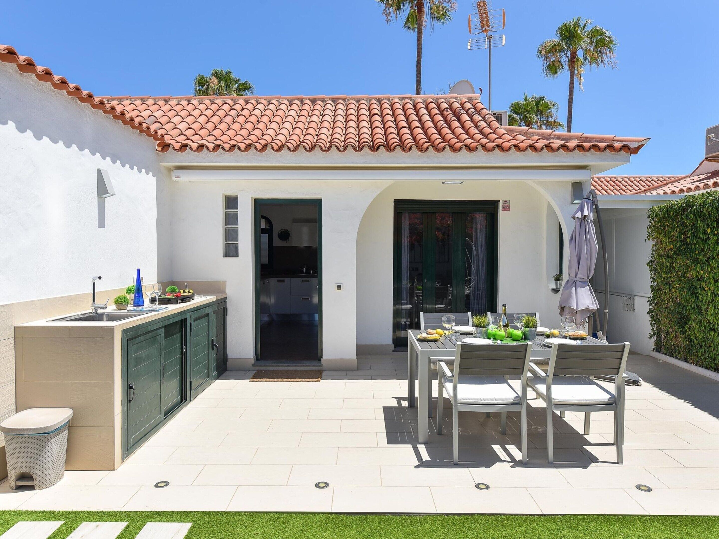 Un patio con mesa y sillas, una pequeña cocina y una puerta que da a un espacio cubierto.