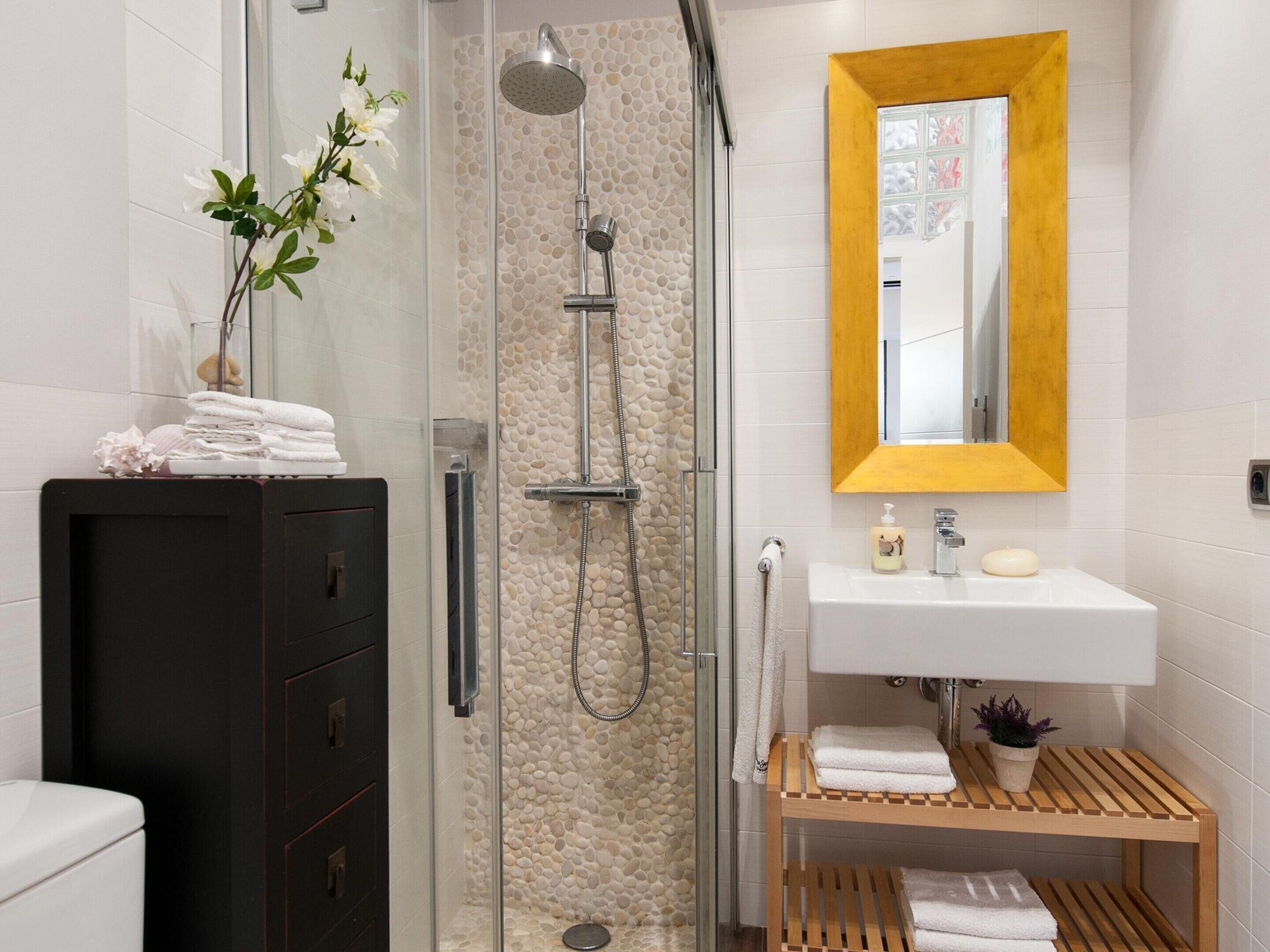 Een moderne badkamer met een douchecabine van glas, witte tegels, een houten wastafelmeubel en een spiegel met een gouden lijst.