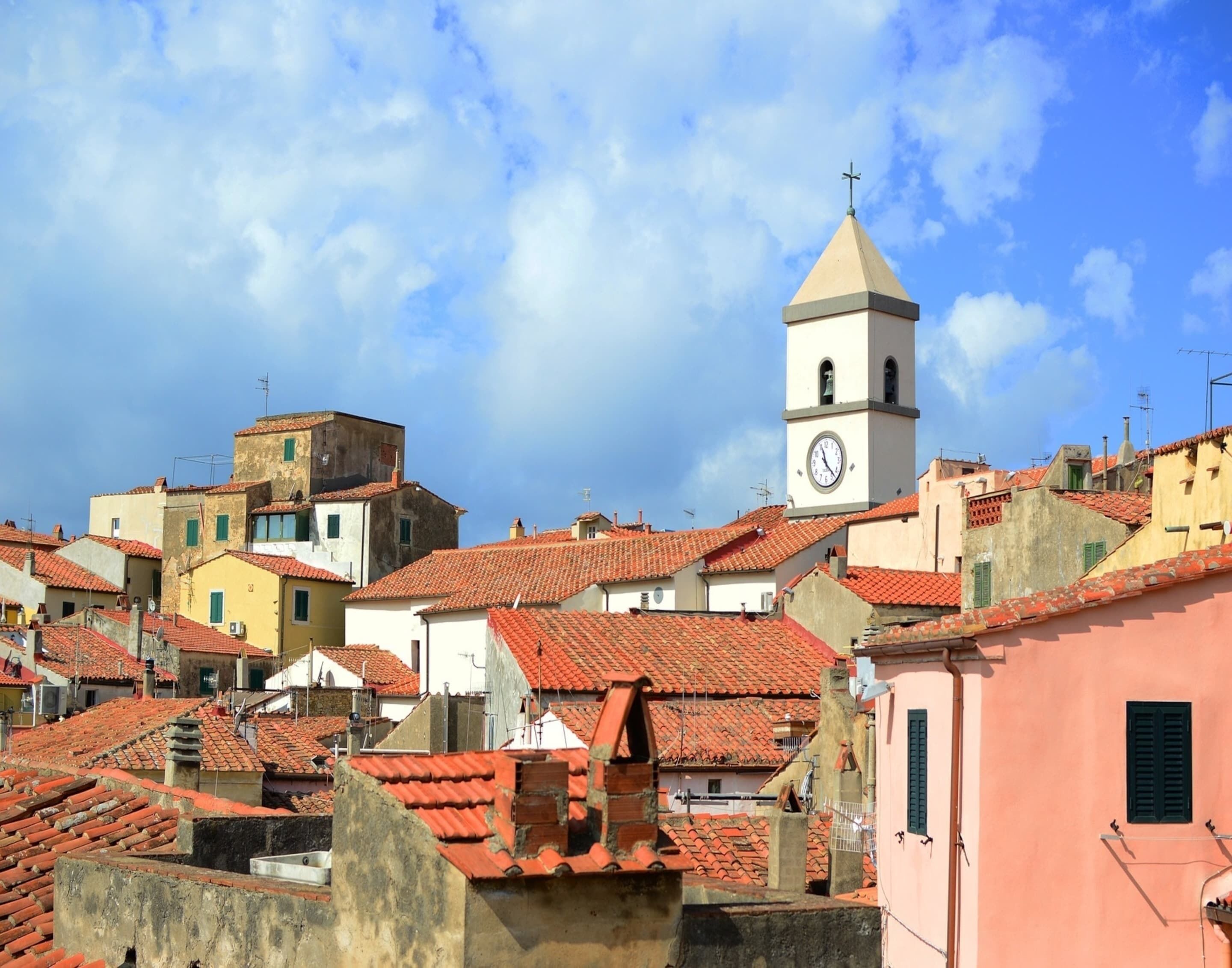 A historic town with red-tiled roofs, a prominent clock tower, and a mix of building styles.
