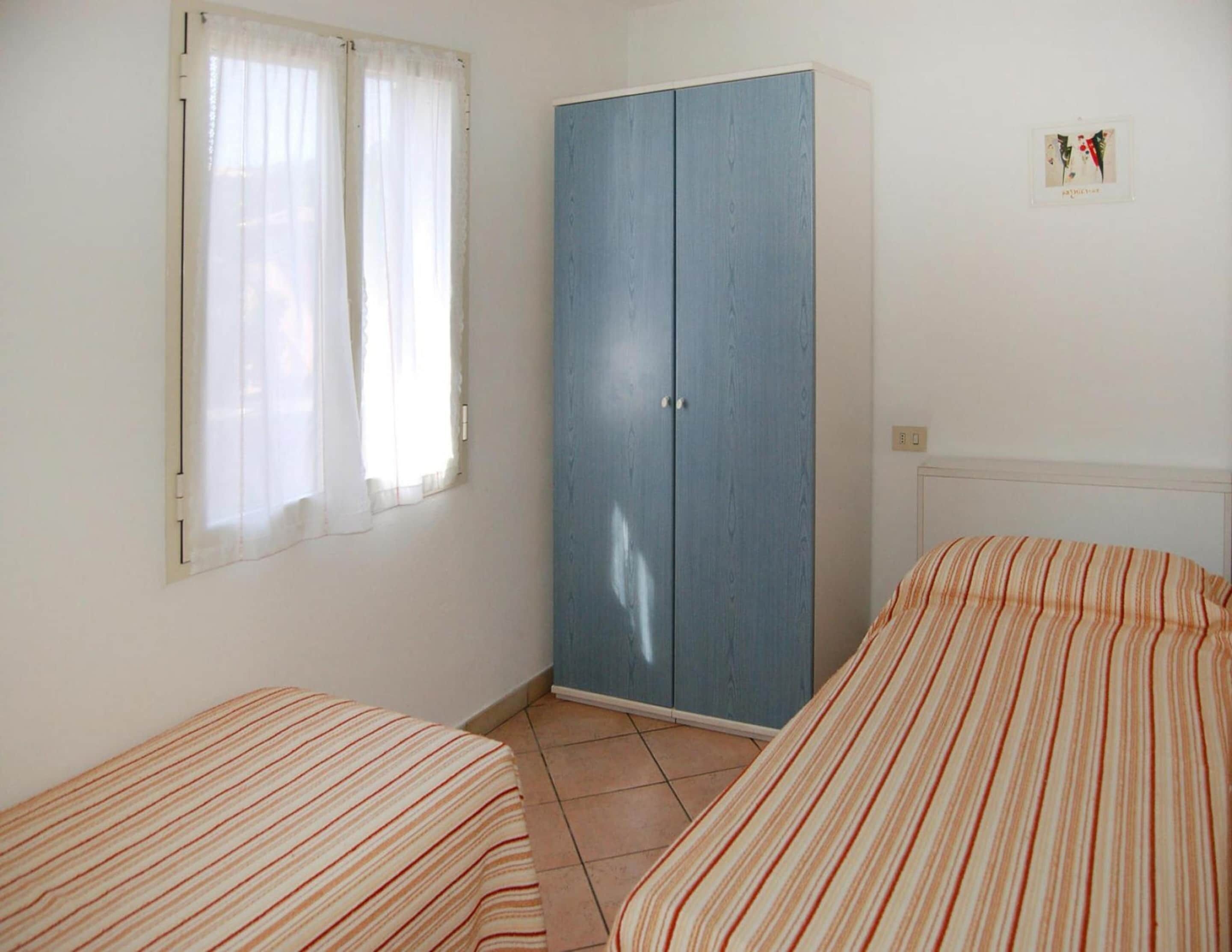 A room with two beds, a wardrobe, and a window with curtains.
