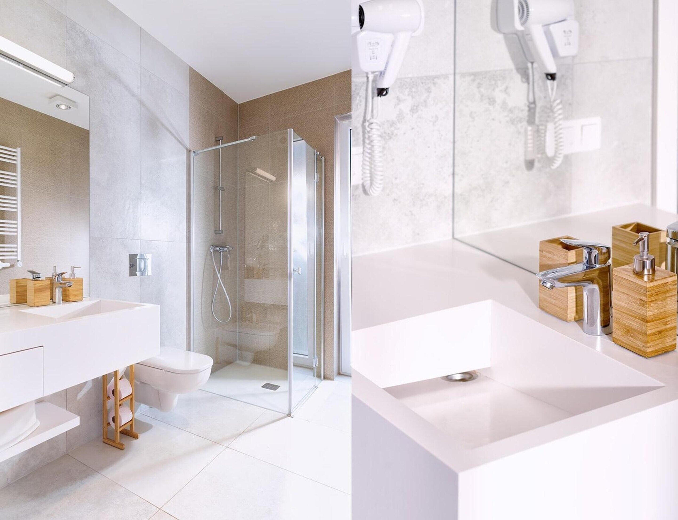 A modern bathroom with a glass-enclosed shower, a white sink with a wooden soap dispenser, and a hairdryer mounted on the wall.
