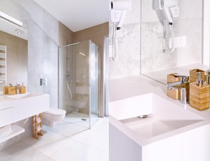 Un bagno moderno con doccia vetrata, lavabo bianco e dispenser per sapone in legno, e un asciugacapelli fissato alla parete.