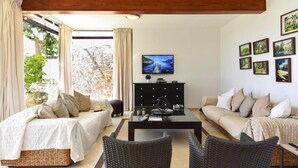 A cozy living room with a sofa, a bed, a coffee table, and a television. There are pictures on the wall and a stone wall outside the window. - Holiday Home in Puerto Rico With Garden (Mogan)
