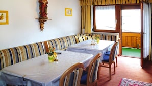 Un coin repas avec des canapés et des tables à rayures, une statue accrochée au mur et, par la fenêtre, une vue sur une terrasse en bois.
