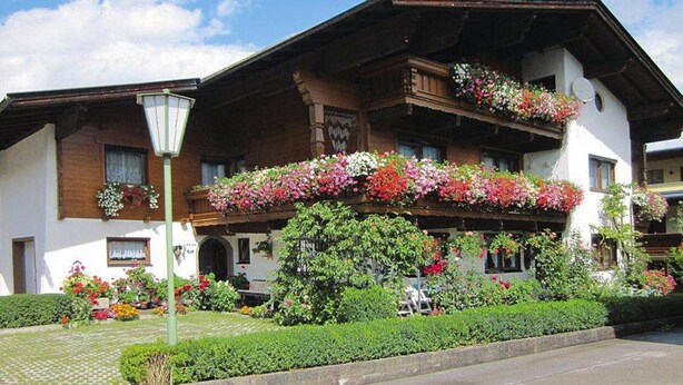 Un chalet traditionnel doté de balcons ornés de fleurs, d’un jardin bien entretenu et surplombant un ciel dégagé.