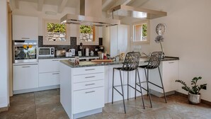 Eine moderne Küche mit weißen Schränken, einer zentralen Kochinsel inklusive Barhocker, einem eingebauten Backofen, einer Mikrowelle und einem Toaster.