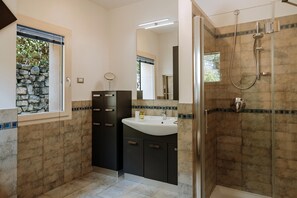 Une salle de bain moderne avec un mur d’accent en pierre, un grand lavabo et une douche à l’italienne.