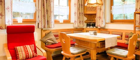 A cozy room with a wooden table and chairs, a red armchair, and a bench with red cushions.