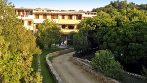 A traditional building with a stone pathway leading to a seating area, surrounded by lush greenery. - Apartment in Porto Rotondo Near Sandy Beach (Olbia)
