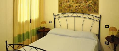 A bedroom with a bed, curtains, a wall tapestry, and two bedside lamps.