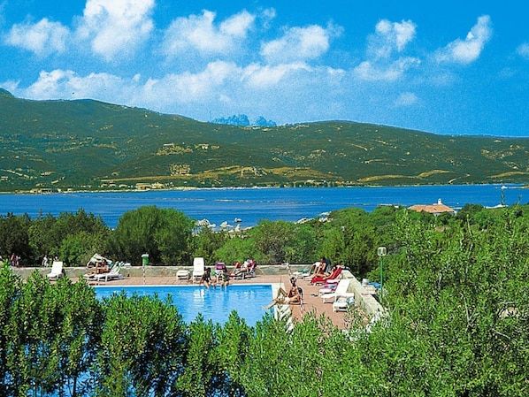 Zona de piscina con sillones de descanso y vistas al mar y las colinas.