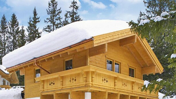 Eine Holzhütte mit Balkon, umgeben von Schnee und Bäumen.