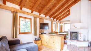 Ein gemütlicher Wohnbereich mit einer Couch, Holzbalken, einem Fernseher und einem Kamin.