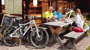Ein hölzerner Essbereich im Freien mit Tisch und Bänken, ein Fahrrad in der Nähe sowie eine Speisekarte an der Wand.